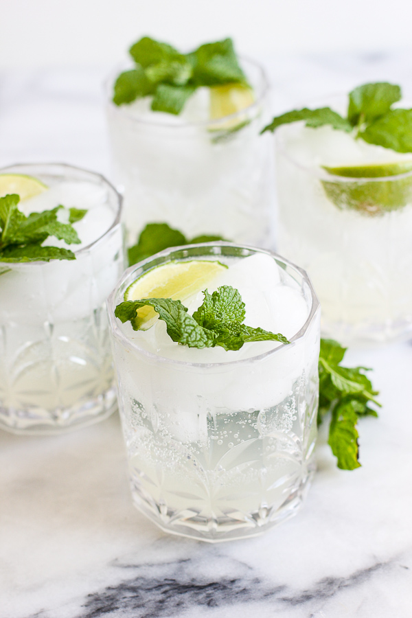 4 mojitos in cocktail glasses garnished with mint and lime