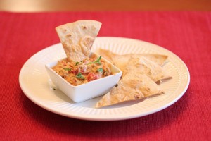 plate with baked tortilla chips and one is dipped in the sausage cheese sauce