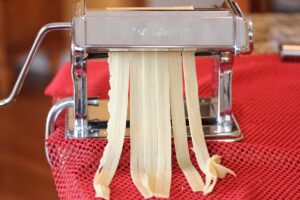 Showing pasta dough as it's being cut into fettuccine noodles