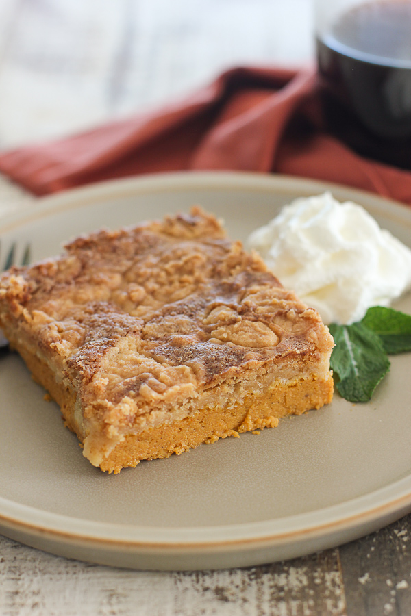 Close up of a slice of pumpkin dump cake served on a plate and garnished with whipped cream and fresh mint