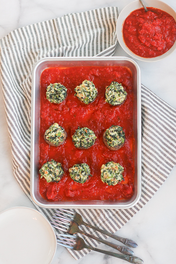 Spinach and Ricotta Stuffed Mushrooms on top of marinara sauce on a sheet pan