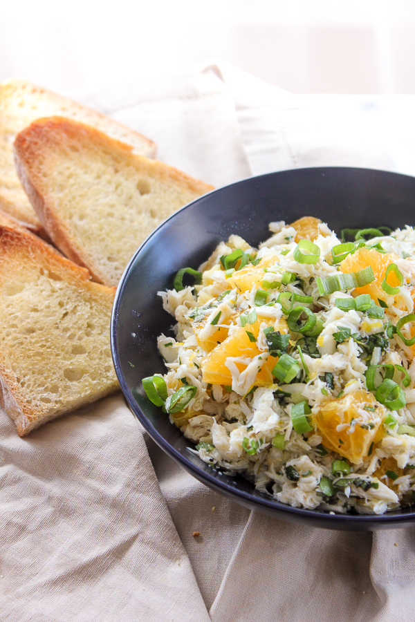 Citrus crab salad in a serving bowl next to pieces of toasted sourdough bread.