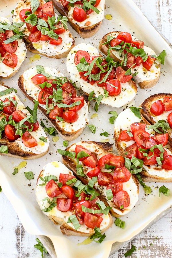 Overhead photo of Warm caprese toast on a sheet pan after topping the melted cheese with the fresh tomatoes and fresh basil