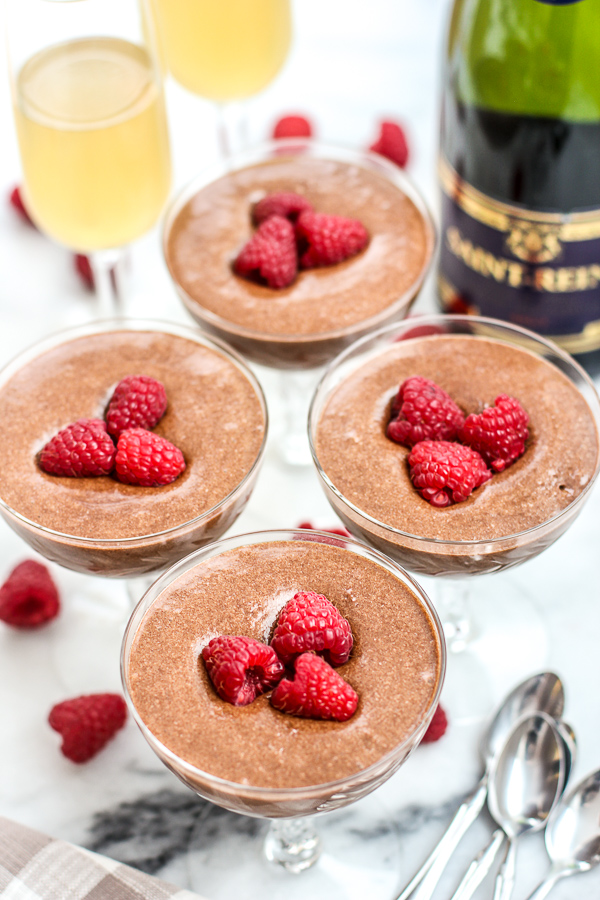 Chocolate mousse in small glass stemmed glasses, garnished with raspberries and served with champagne